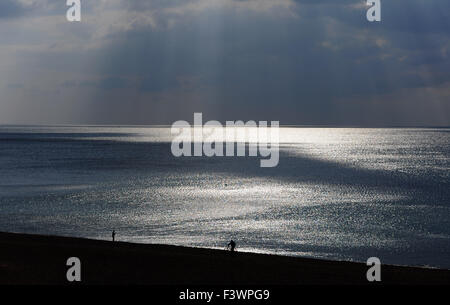 Brighton, Regno Unito. 13 ottobre, 2015. Un uomo spinge la sua bicicletta lungo la spiaggia come alberi di rompere la luce del sole attraverso le nuvole scure che si stanno formando off Brighton oggi il tempo è impostato in modo da diventare più instabile nei prossimi giorni di credito: Simon Dack/Alamy Live News Foto Stock