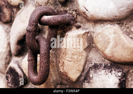 Catena arrugginito appeso sul vecchio muro di pietra Foto Stock