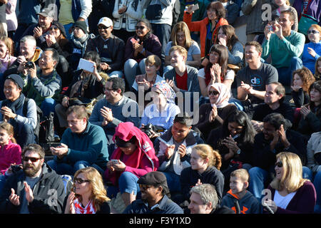 Un gruppo di persone multietniche di tutte le età, ampio e diversificato, che si siedono all'esterno su bleachers in cemento che reagiscono a guardare artisti di strada che si esibiscono negli Stati Uniti Foto Stock