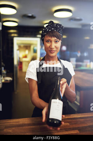 Sorridente giovane cameriera presentando una bottiglia di vino rosso a un cliente per approvazione prima di aprirlo, concettuale di un giovane piccolo Foto Stock