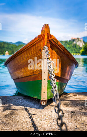 Dettaglio del legno ancorata la barca turistica sulla riva del lago di Bled, Slovenia con il castello di Bled in background Foto Stock