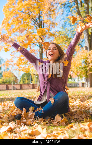 Felice donna seduta su un terreno la riproduzione di foglie secche Foto Stock