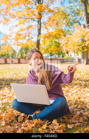 Felice donna seduta su foglie essiccate con il computer portatile Foto Stock