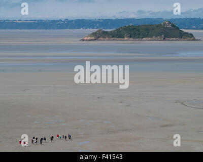 Gruppo di turisti a piedi attorno a Mont Saint Michel in bassa marea con un isola in background Foto Stock