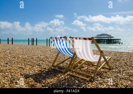 Due sedie a sdraio sulla spiaggia unico a Brighton e Hove con i resti del molo Ovest in distanza, East Sussex, Inghilterra. Foto Stock