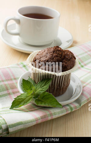 Muffin al cioccolato bianco sul piatto con il rametto di menta tovagliolo di lino e un cappuccio di tè. Messa a fuoco selettiva Foto Stock