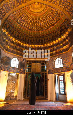 Tomba santuario, pellegrino vestito di nero chador nelle altamente decorato hall di ingresso alla camera tomba, Qandil Kaneh Foto Stock