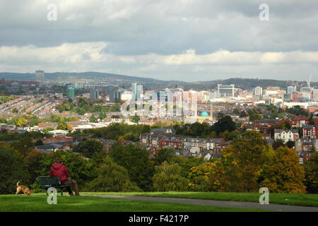 Un uomo con un cane di pause nel Meersbrook Park per visualizzare lo skyline della città di Sheffield South Yorkshire England Regno Unito - autunno Foto Stock