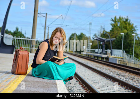 Donna seduta sulla stazione e la lettura Foto Stock