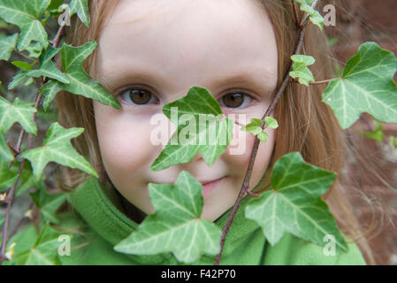 Bambina cerca attraverso ivy, close-up Foto Stock