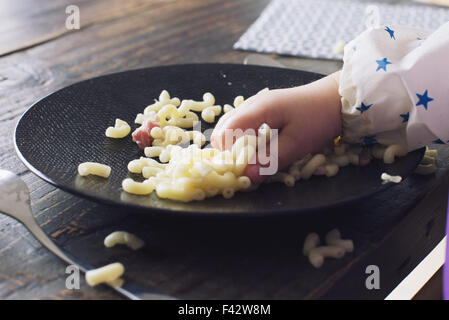 Bambino mangiare maccheroni con la sua mano, ritagliato Foto Stock