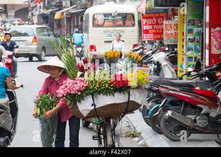 Signora vietnamita venditore di fiori nel quartiere vecchio di Hanoi, che vendono fiori dal retro della sua bicicletta.Vietnam Foto Stock