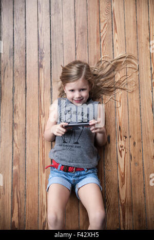 Bambina giacente sul piano utilizza lo smartphone Foto Stock