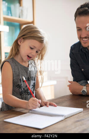 Padre guarda la giovane figlia pratica di scrittura Foto Stock