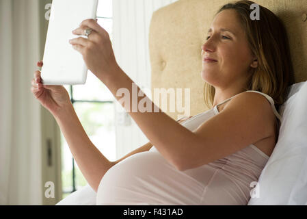 Donna incinta con tavoletta digitale per una chat video con amici e familiari Foto Stock