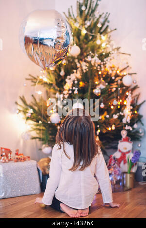 Ragazza seduta sul pavimento fissando lo sguardo fino ad albero di Natale Foto Stock