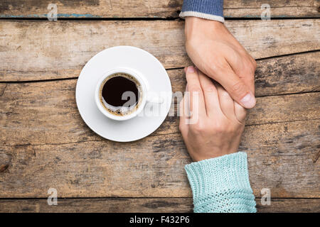 Uomo Donna mantiene la mano con tazza di caffè vista dall'alto immagine sullo sfondo di legno. Amicizia sullo sfondo di caffè Foto Stock