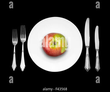 Red apple su piastra bianca con coltello e forchetta, vista dall'alto su sfondo nero Foto Stock