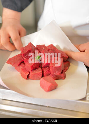 Butcher avvolgere carni cubi in carta oleata, ritagliato Foto Stock