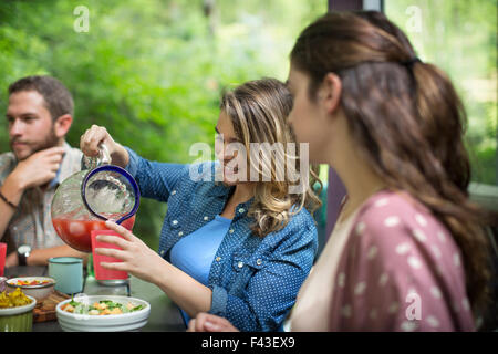 Tre persone sedute a un tavolo nel bosco, avente un pasto, una donna colata di succo da una caraffa. Foto Stock