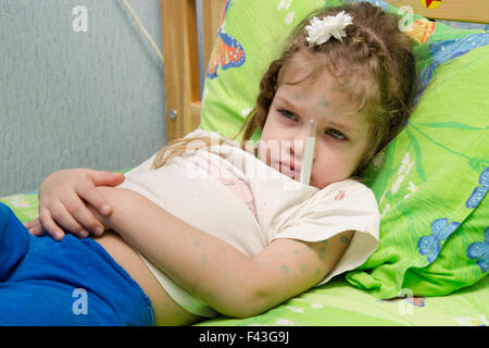 Bambina giacente in letto con un termometro Foto Stock