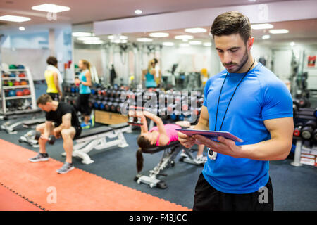 Bello il trainer utilizzando tablet in sala pesi Foto Stock