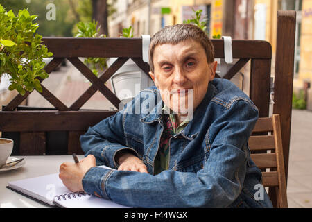 Adulto Uomo disabili con paralisi cerebrale seduto con un notebook a un cafe' all'aperto. Foto Stock
