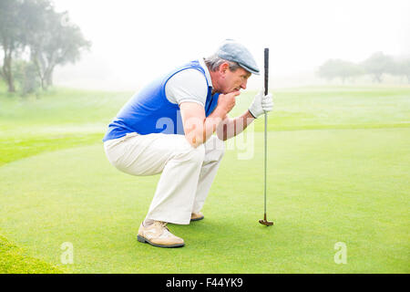 Grave golfista inginocchiato sul putting green Foto Stock