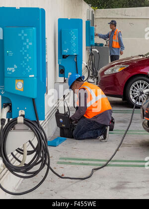 Tecnico di riparazione mantiene un auto elettrica stazione di ricarica a un Irvine, CA, ospedale parcheggio. Nota auto elettrica essendo caricato a destra. Foto Stock