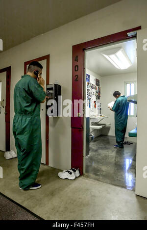 Uniformata ispanica detenuti adolescenti di un'arancia, CA, carcere minorile utilizzare un telefono a pagamento e leggere nella loro cella. Nota mancanza di barre. Foto Stock