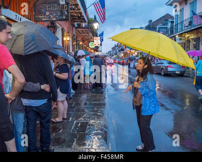 Huddling sotto gli ombrelli sotto la pioggia su San Pietro Street a New Orleans, gli amanti del jazz di attendere in linea per immettere la città famosa Preservation Hall sala musicale. Foto Stock