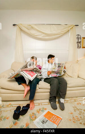 Due teen boys ispanica leggere le sezioni di un giornale comodamente seduti sul divano di casa in Santa Ana CA. Foto Stock