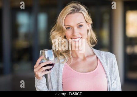 Ritratto di sorridere donna bionda permanente e la holding wineglass Foto Stock