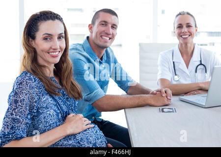 Medico e futuri genitori sorridente in telecamera Foto Stock