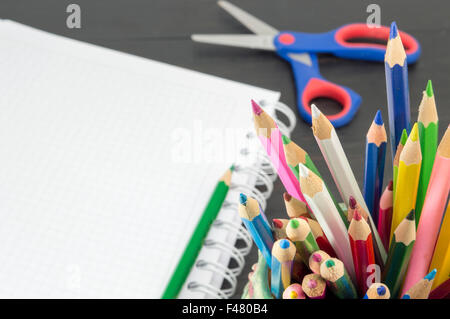 Lavorare con matite colorate. Matite colorate nel vaso con un notebook in background Foto Stock