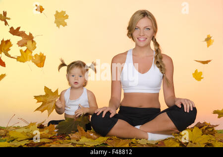 Donna e bambino a praticare lo yoga sotto le foglie Foto Stock