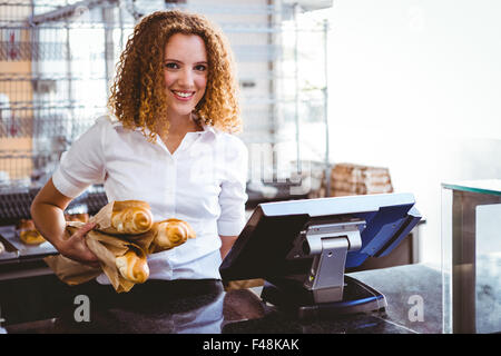 Piuttosto barista utilizzando un registratore di cassa e la holding della pagnotta di pane Foto Stock