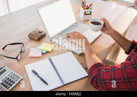 Mani digitando su laptop e contenimento di bevande calde Foto Stock