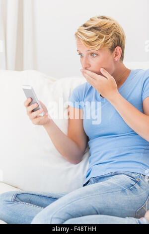 Sorpreso donna seduta sul lettino e guardando a smartphone Foto Stock