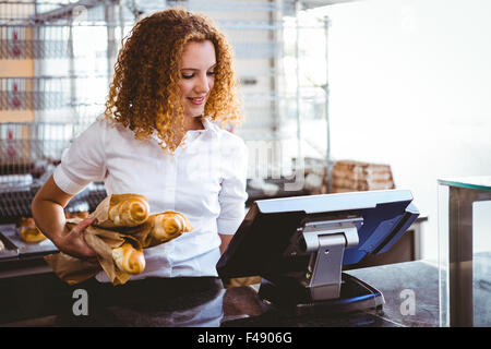 Piuttosto barista utilizzando un registratore di cassa e la holding della pagnotta di pane Foto Stock