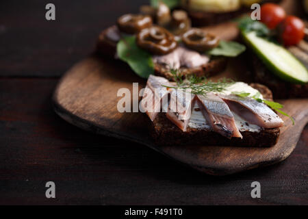 Varietà di aprire panini di dense imburrato, scuro pane di segale con diversi condimenti. Smorrebrods danese su uno sfondo di legno. Né Foto Stock