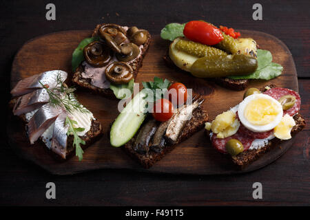 Varietà di aprire panini di dense imburrato, scuro pane di segale con diversi condimenti. Smorrebrods danese su uno sfondo di legno. Né Foto Stock