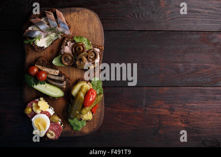 Varietà di aprire panini di dense imburrato, scuro pane di segale con diversi condimenti. Smorrebrods danese su uno sfondo di legno. Né Foto Stock