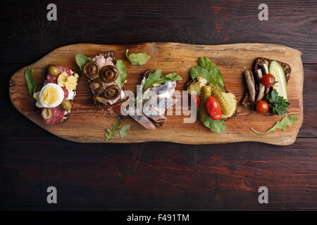 Varietà di aprire panini di dense imburrato, scuro pane di segale con diversi condimenti. Smorrebrods danese su uno sfondo di legno. Né Foto Stock