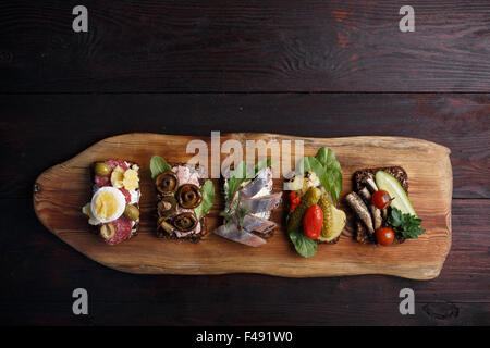 Varietà di aprire panini di dense imburrato, scuro pane di segale con diversi condimenti. Smorrebrods danese su uno sfondo di legno. Né Foto Stock