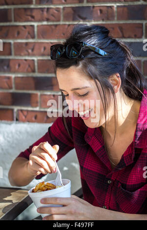 Felice giovani donne mangiare poutine quebec pasto fast food all'aperto nelle ore diurne Foto Stock