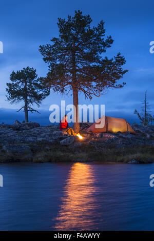 L'uomo con il fuoco e la tenda accanto a un lago, Svezia Foto Stock