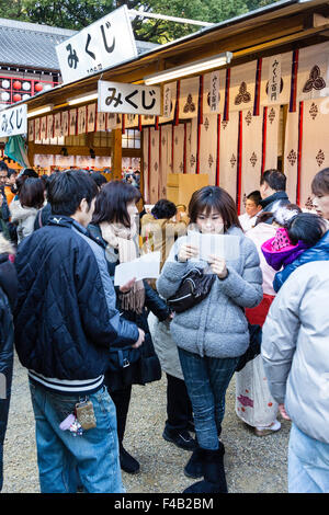 Giappone, Nishinomiya santuario, Capodanno, Shogatsu. Due giovani donne e giovani man standing insieme, lettura Omukuji fortune paper. Foto Stock