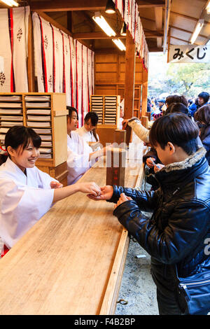 Giappone, Nishinomiya santuario, anno nuovo giorno, Shogatsu. Donna acquisto omikuji fortune paper da Miko, santuario maiden, al santuario di occupato ufficio, Shamusho. Foto Stock