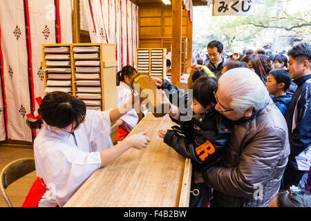 Giappone, Nishinomiya santuario, anno nuovo giorno, Shogatsu. Donna acquisto omikuji fortune paper da Miko, santuario maiden, al santuario di occupato ufficio, Shamusho. Foto Stock